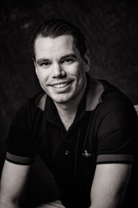 Black & white portrait of a short haired man leaning towards the camera