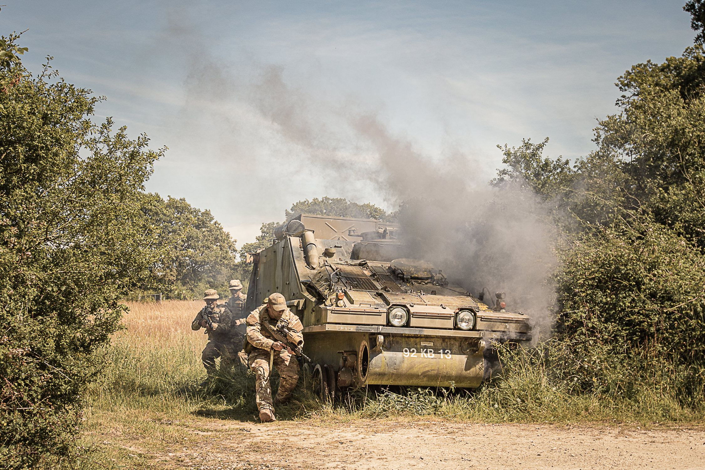 Uk Army soldiers criuched near a smoking military vehicle