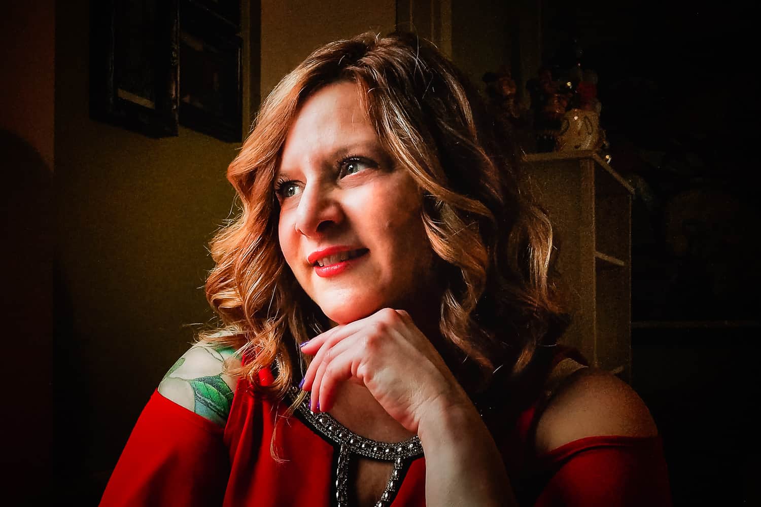 Remote portrait of a woman wearing a red top looking out of her window with her hand under her chin. Taken remorely by Pixellit Commercial photography