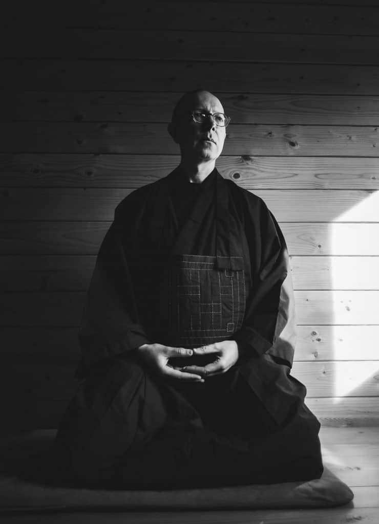 Black & white image of Kneeling man wearing budhist robes in meditation.